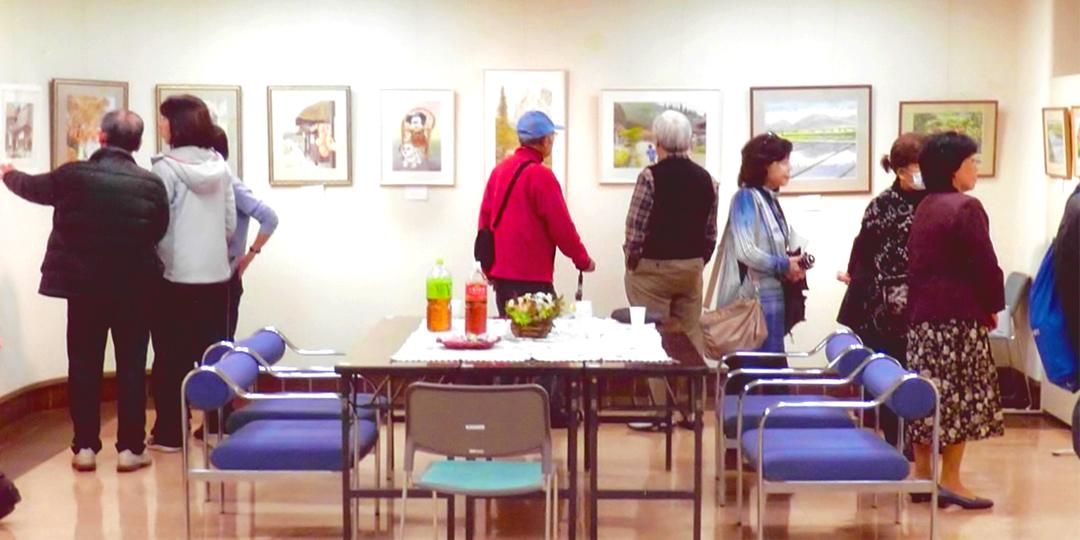 壁に水彩画の作品が多数展示されており、来館者の方々が作品の前に立ち止まって、絵画を鑑賞している写真
