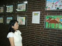 市庁舎の壁面に展示されている児童が描いた絵画を女性が見ているアップ写真