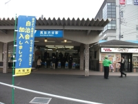 駅の改札の前で、緑色の上着を着た男性がスーツを着た男性の目の前に立っている写真
