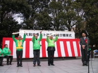 黄緑色のジャンパーを着た男性3人が青色防犯パトロールカーの鍵を両手で上に挙げてる写真