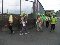 黄緑の帽子に反射ベストを着た方々が誘導灯を持って防犯パトロールする写真