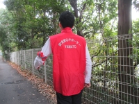 大和市安全安心サポーターの赤色のベストを着用した男性が歩道をパトロールしている後ろ姿の写真