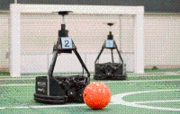 奥にサッカーゴールがあるフィールドに、2体のサッカーロボットがある写真