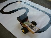 自動車型ロボットが黒い線が引かれた上を走っている写真