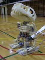 体育館のような床に置かれた恐竜の化石のロボットの写真