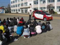 校庭で電気自動車の説明を聞いている生徒たちを後ろから写した写真