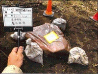 四角で茶色のビニール袋の角に4つの土嚢が置かれ、証明資料を撮影している写真