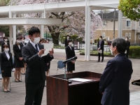 後ろには桜が咲いていて、新採用職員が並び、代表者が挨拶する写真
