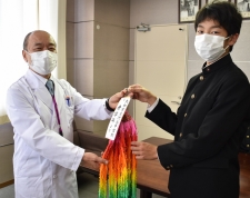 学生服を着た渋谷中学校3年生が白衣を着た先生へ千羽鶴を贈る写真