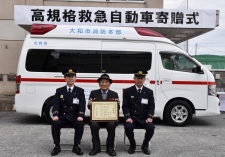 救急車の前に救急隊員2人と戸澤(とざわ) 章(あきら)さんが感謝状を持って記念写真
