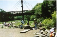 大きなつり橋のある河川敷でキャンプを楽しんでいる人々の写真