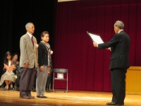 ステージ上で2名の男女が右側の男性から表彰状を授与されている様子の写真