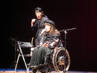 マイクの前で車いすに乗って話す萩生田氏と斜め後ろで手話をしている女性の写真