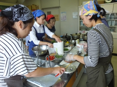 カラフルな三角巾をした5名の女性が各担当の自料理をしている写真