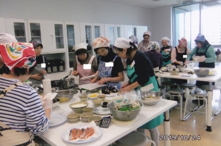 机に乗せられた鮭やボールに入った野菜を使い調理実習をしている参加者の人達の写真