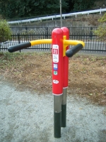赤色の棒に黄色のアームが付いている健康遊具スイスイ屈伸の写真