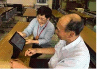 男性職員が机の上の液晶画面を見せながら高齢者男性に話をしている写真