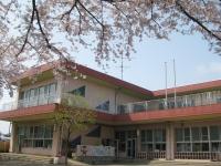 桜の咲いている園庭から見える茶色い屋根2階建ての福田保育園の外観写真