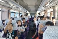 参加者の子供達がバスの中で手を挙げている写真