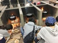 子供たちがダッチオーブンの下で薪を組み火を起こしている野外炊事の様子の写真