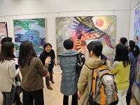 美術館内に並んでいる絵画の前で女性が話しているのを参加者たちが聞いている写真