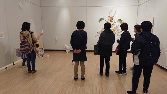 展示されている白色の小さな小人の形をした作品などを鑑賞している人達の写真