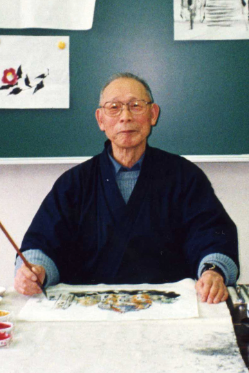 作品の前に座り、筆を持っている本吉 薫 氏の写真