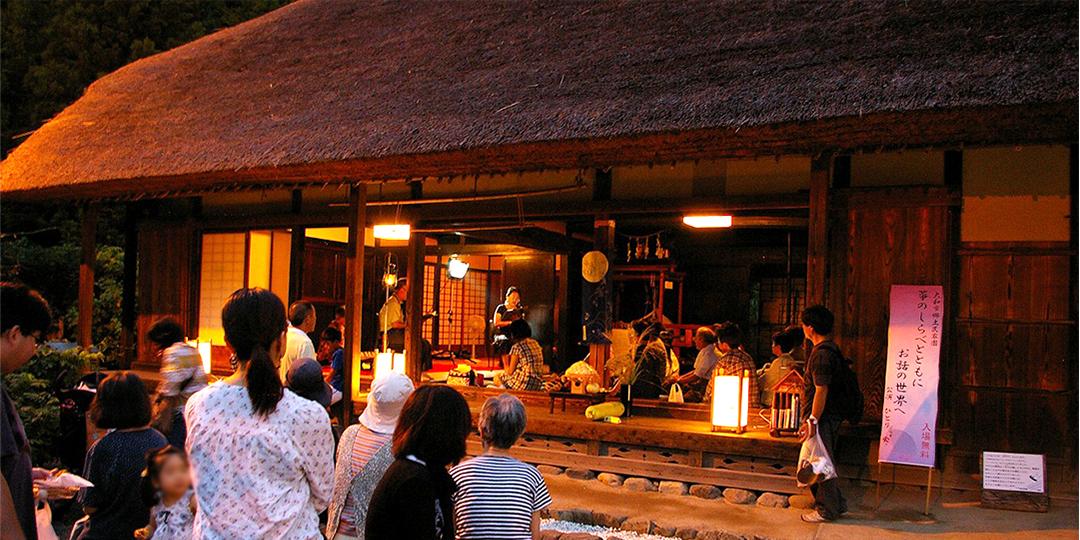 茅葺屋根の一軒家で演劇が披露されているのを観覧車が観ている後ろ姿の写真