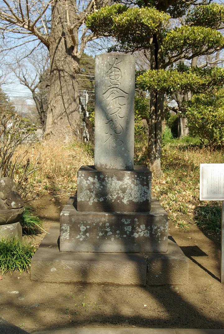 右側に立て看板、中央に石塔で作られた徳本念仏塔、その後ろに木々が写っている写真