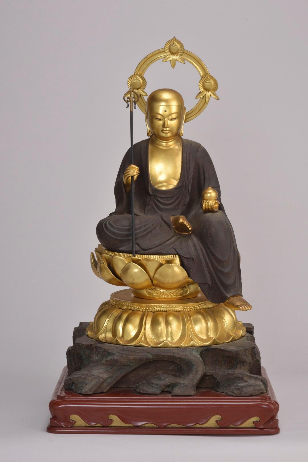 黄金色の仏像が蓮の台座に座り、左手に宝珠、右手に錫杖を持っている写真