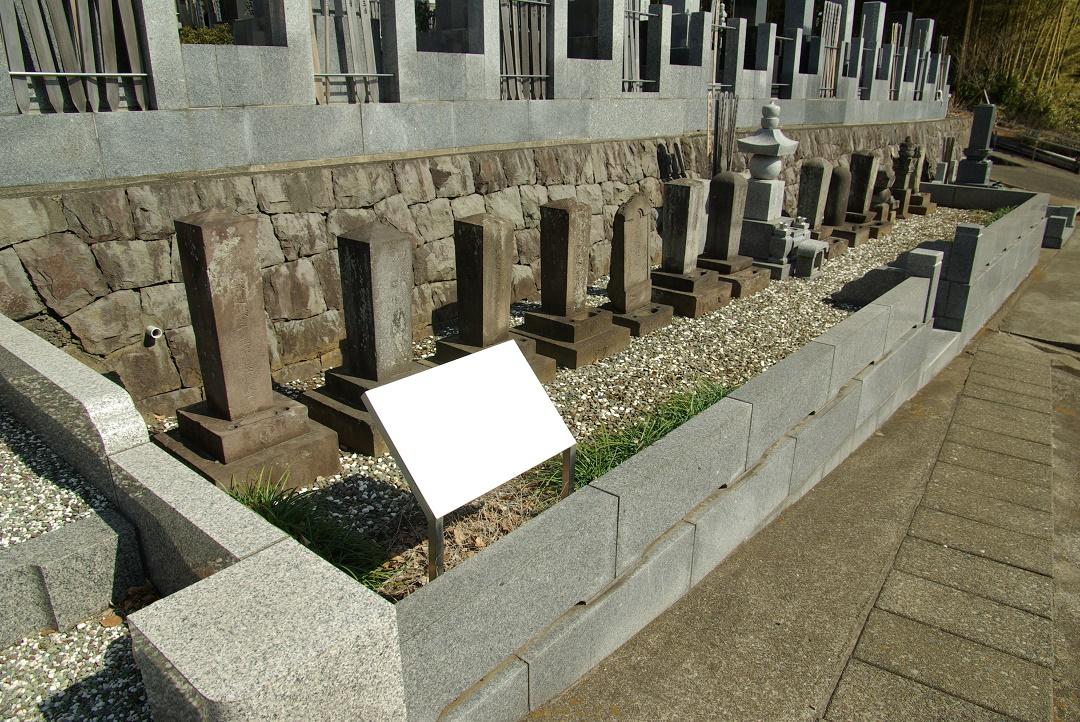 墓碑や供養塔の前に白いプレートが置かれた旧石川家墓地の写真