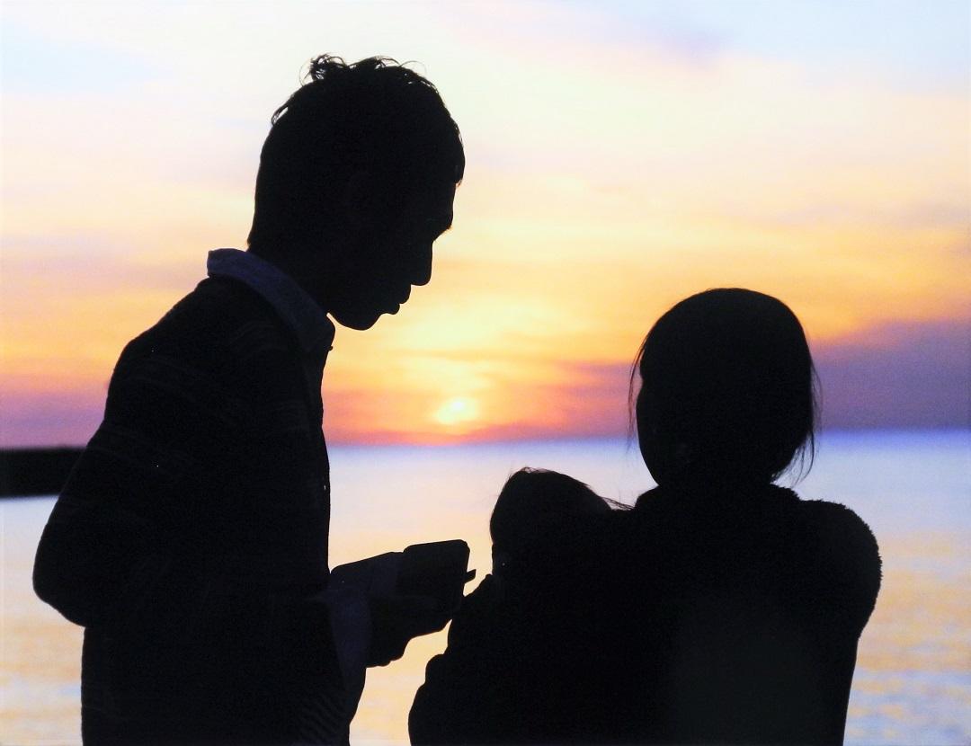 綺麗な夕日の見える海をバックに赤ちゃんを抱いた両親が写っている写真