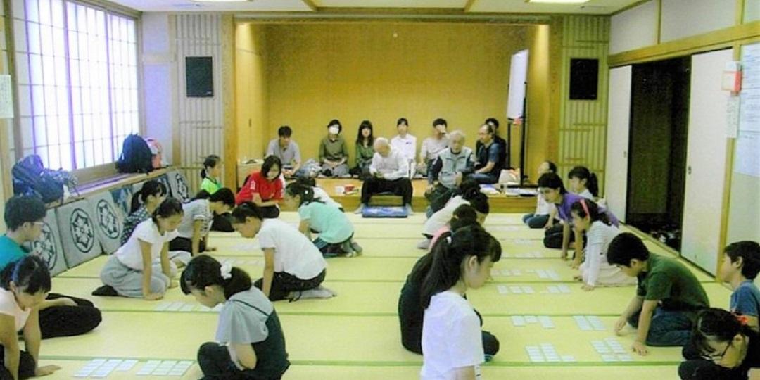 和室の畳の上にかるたを並べて、対面に座っている子ども達が、真剣な表情で並んだ札を見て百人一首競技かるたをしている様子の写真