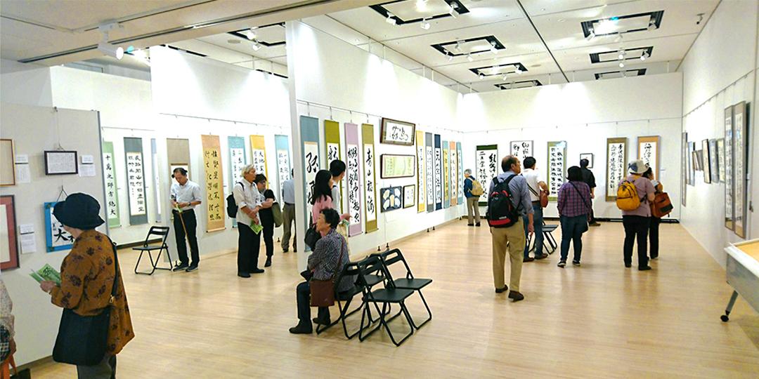 ギャラリーに展示されている書の作品がを見に来ている人々の写真