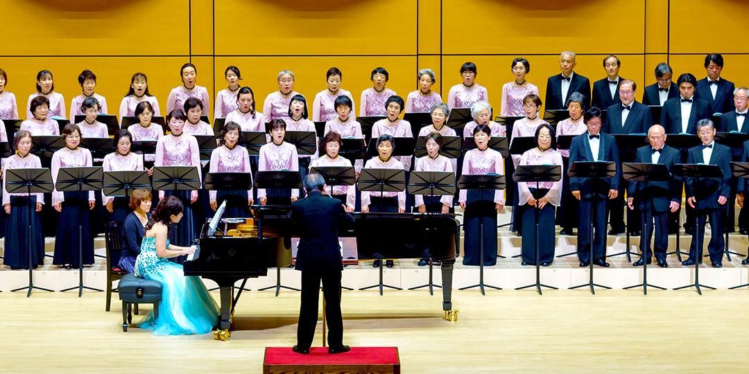 ピアノの伴奏で横3列に並んだ大和混声合唱団が歌を披露している写真