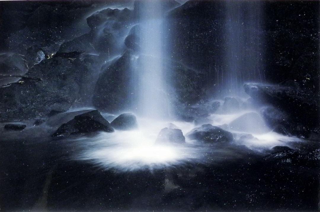 暗闇の中の岩場に真上から勢いよく落ちてくる滝の水の流れや飛沫がが白く浮かび上がっている写真