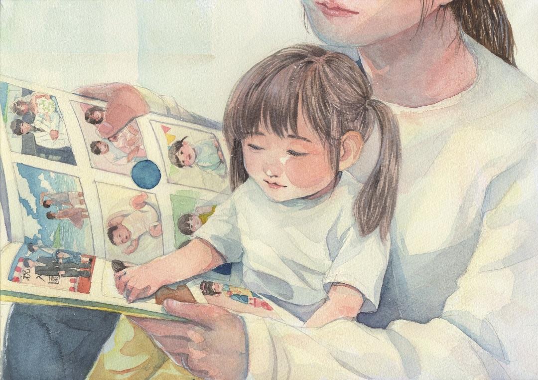 女の子が母親の膝の上に座りアルバムを一緒に見ている様子を描いた「あたたかい時間」の写真