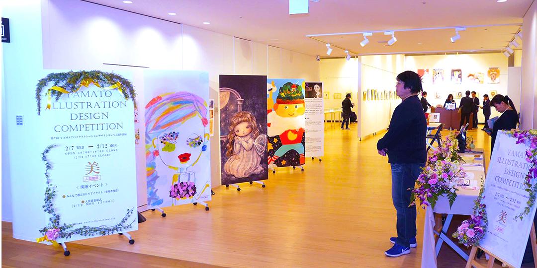 大きなボードに描かれた作品が会場受付前に並んで展示されており、奥にも沢山の作品が壁に並んで展示されている絵画展会場の写真