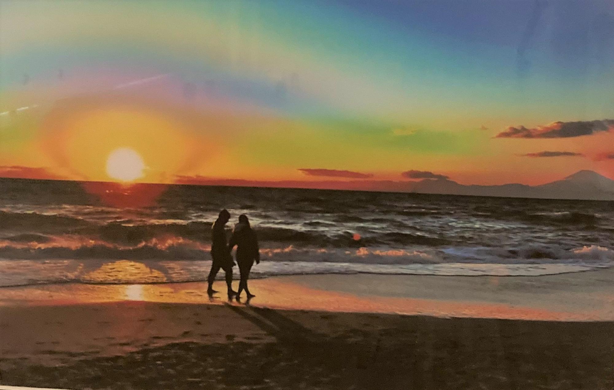 海で夕焼けに照らされて歩いている2名の後ろ姿の写真