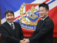 横浜マリノスの旗の前で古川宏一郎代表取締役社長と市長が両手で握手をしている写真