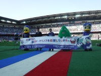 横浜マリノスのホームタウンの芝の上でマリノスのマスコットキャラクター2体とヤマトン、男性2名で横断幕を持っている写真