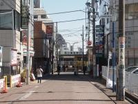 道路の左右に店舗が入っているビルがあり、その間を歩く通行人の写真