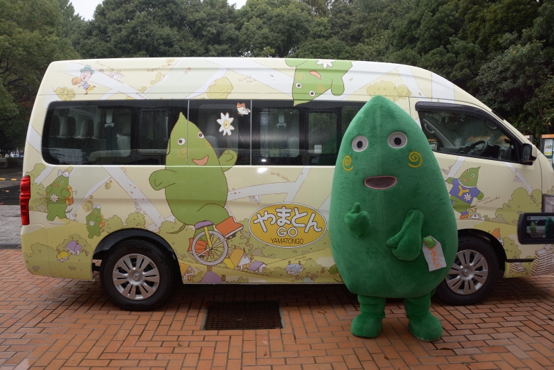 車体にヤマトンのイラストが描かれたバスの前に立っているヤマトンの写真