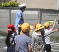 手を挙げて横断歩道を渡る児童たちを横断旗で誘導している様子の写真