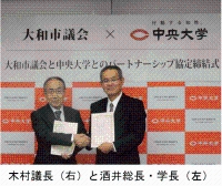 木村議長と酒井正三郎総長・学長が協定書を持って、固く握手をしている写真