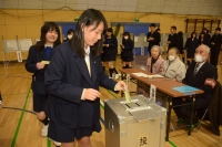 体育館で女子生徒が投票箱に表を投じている写真