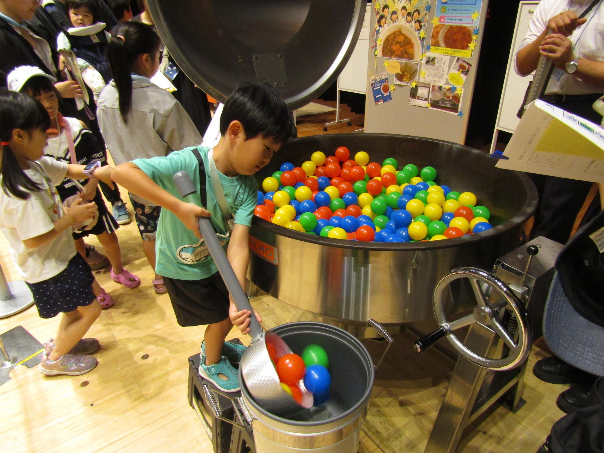 給食の大きな回転釜から、プラスチックのボールを食缶に移し替えている男の子