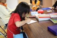 女の子が机に座り紙に何かを書いている写真