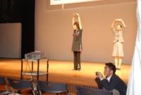 舞台の上で両手をあげ丸をつくるポーズをする女性2名の写真