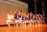 舞台の上で白や紫のハッピを着て阿波踊りを披露している写真
